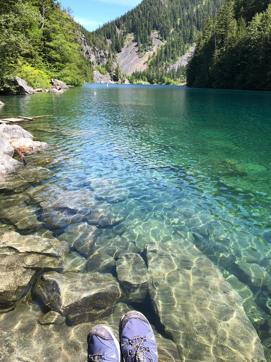 A pair of hiking boots being worn by someone sitting at the edge of Lindeman Lake.